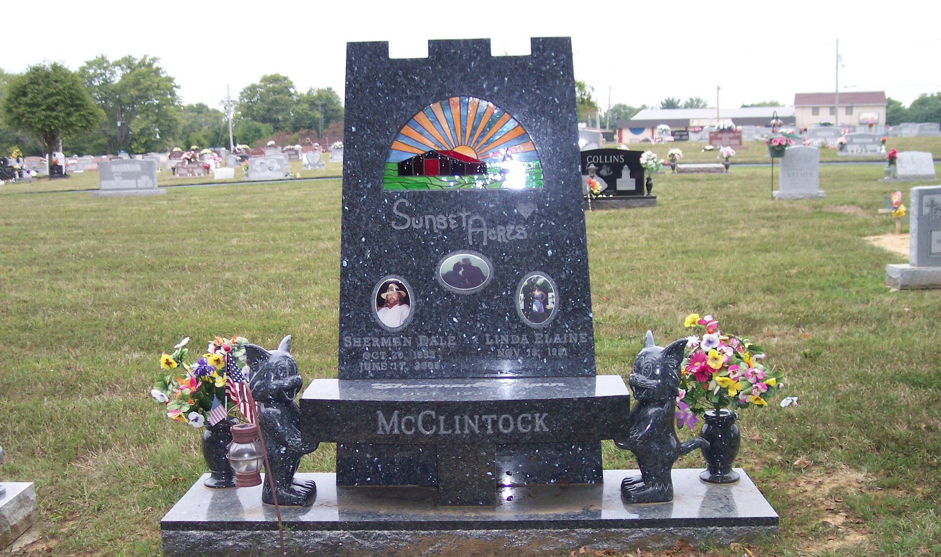 Black memorial headstone with rainbow design and flower bouquets in a cemetery
