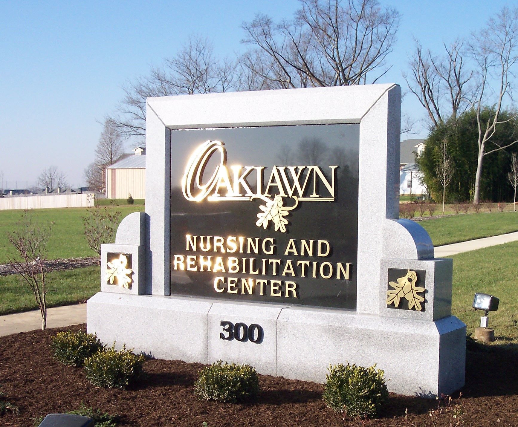 Stone sign for Oaklawn Nursing and Rehabilitation Center with landscaping and blue sky.
