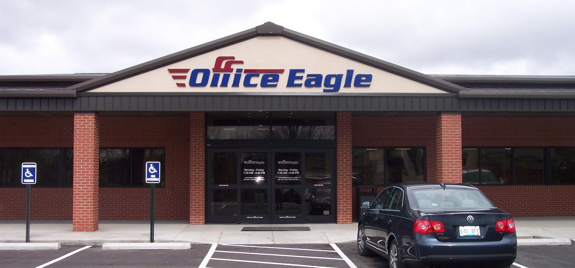 Office Eagle storefront with brick columns and a parked black car in front