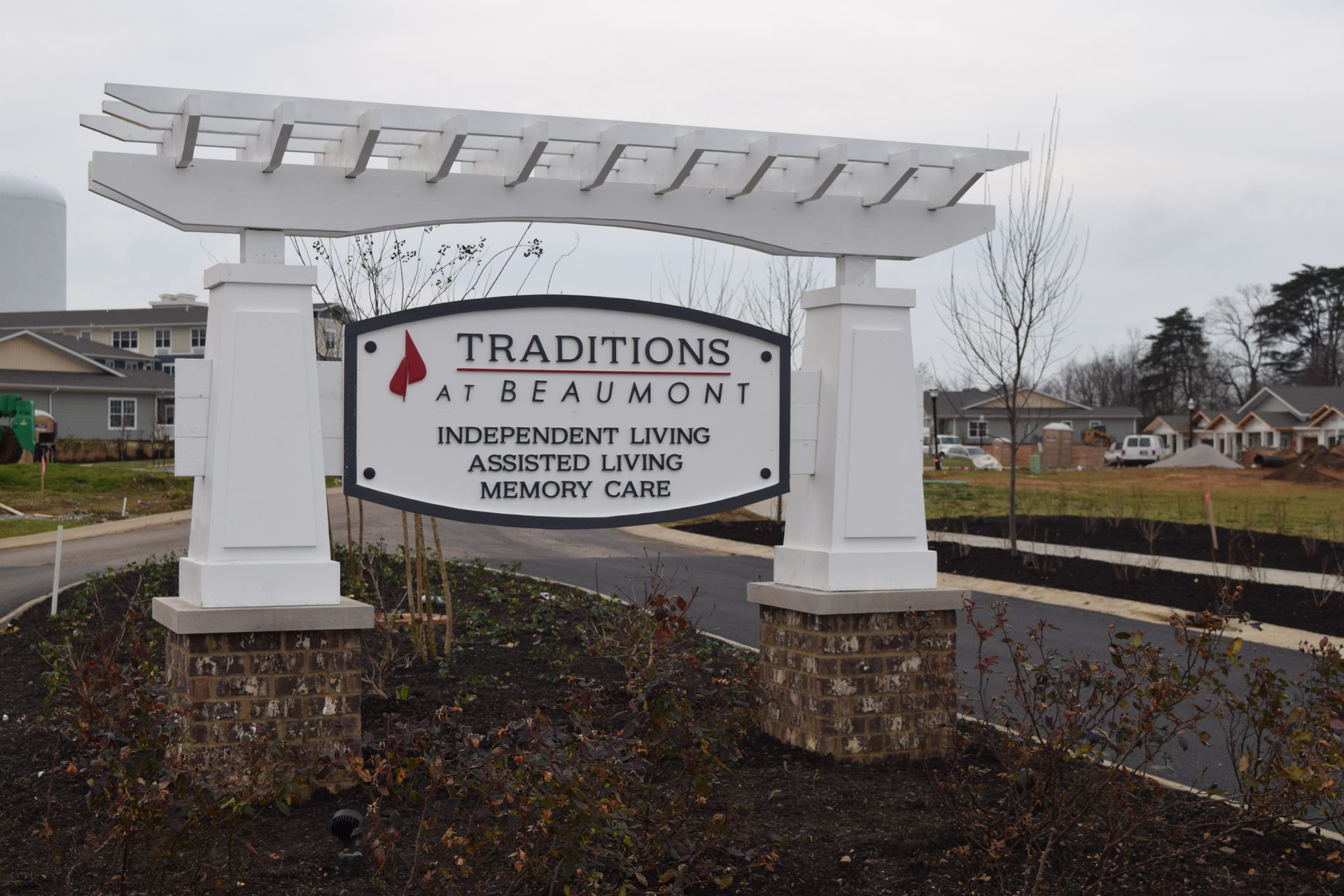 Traditions at Beaumont entrance sign beneath a white pergola, beside a landscaped road