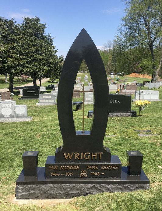 Black Wright gravestone monument in a cemetery, with trees and other headstones behind it.