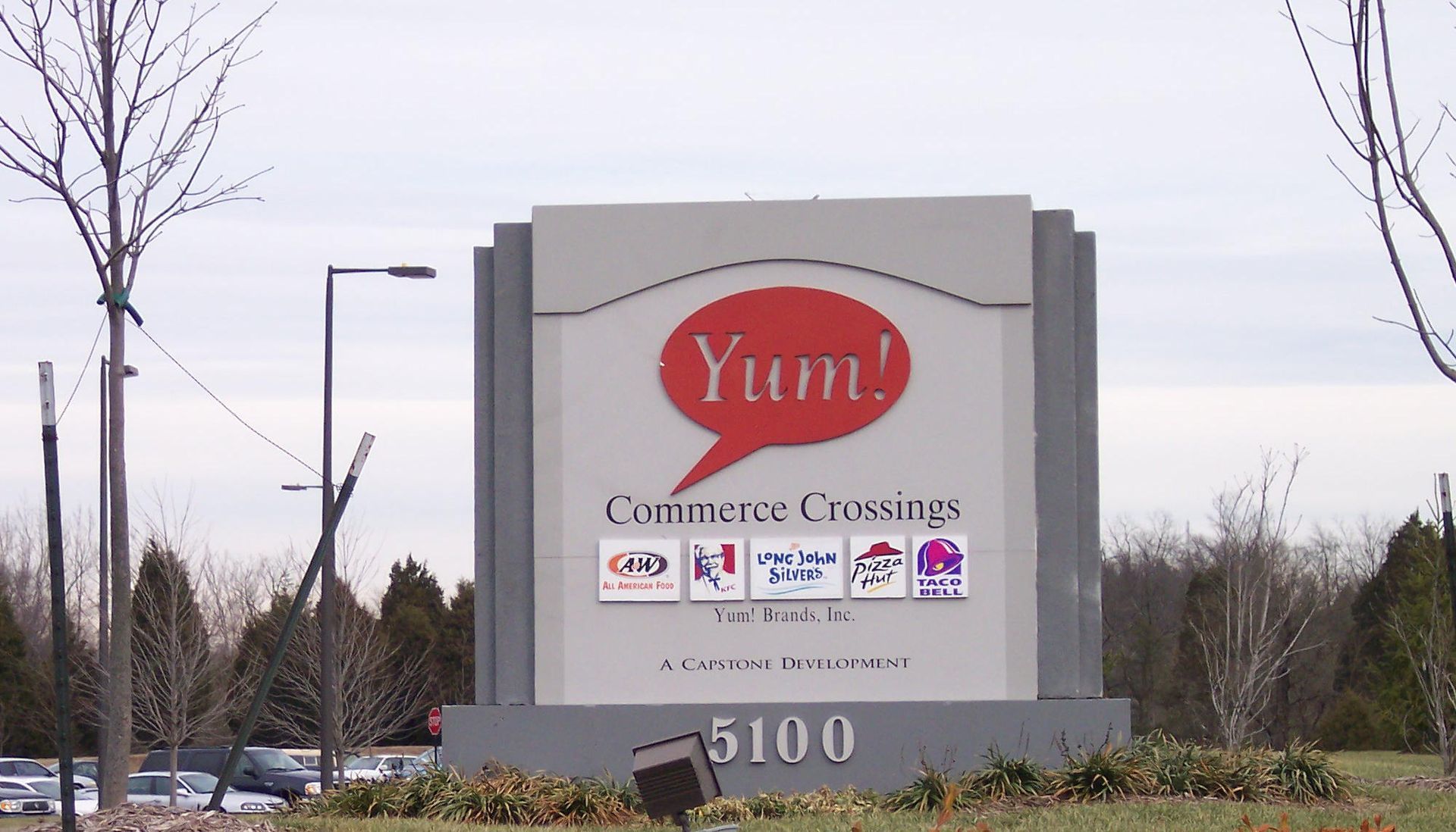 Roadside sign for Yum! Custom Creations at 5100, with red logo and small brand icons.
