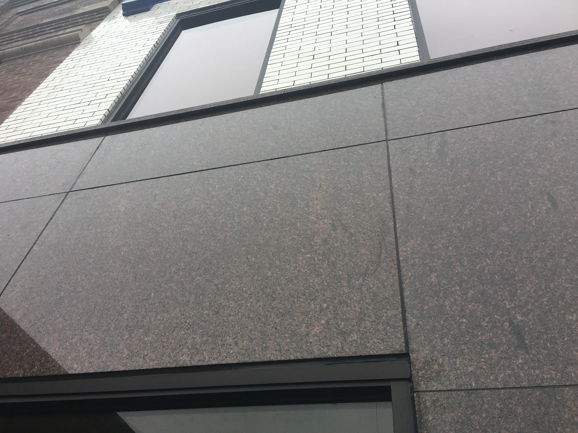 Low-angle view of a gray building facade with windows and stone panels