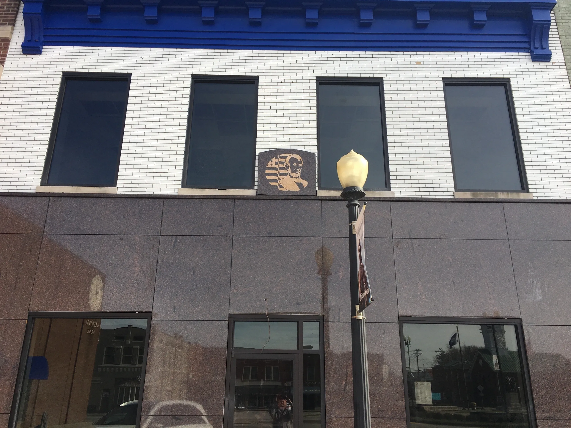 Storefront with dark windows, white brick upper facade, and a streetlamp in front