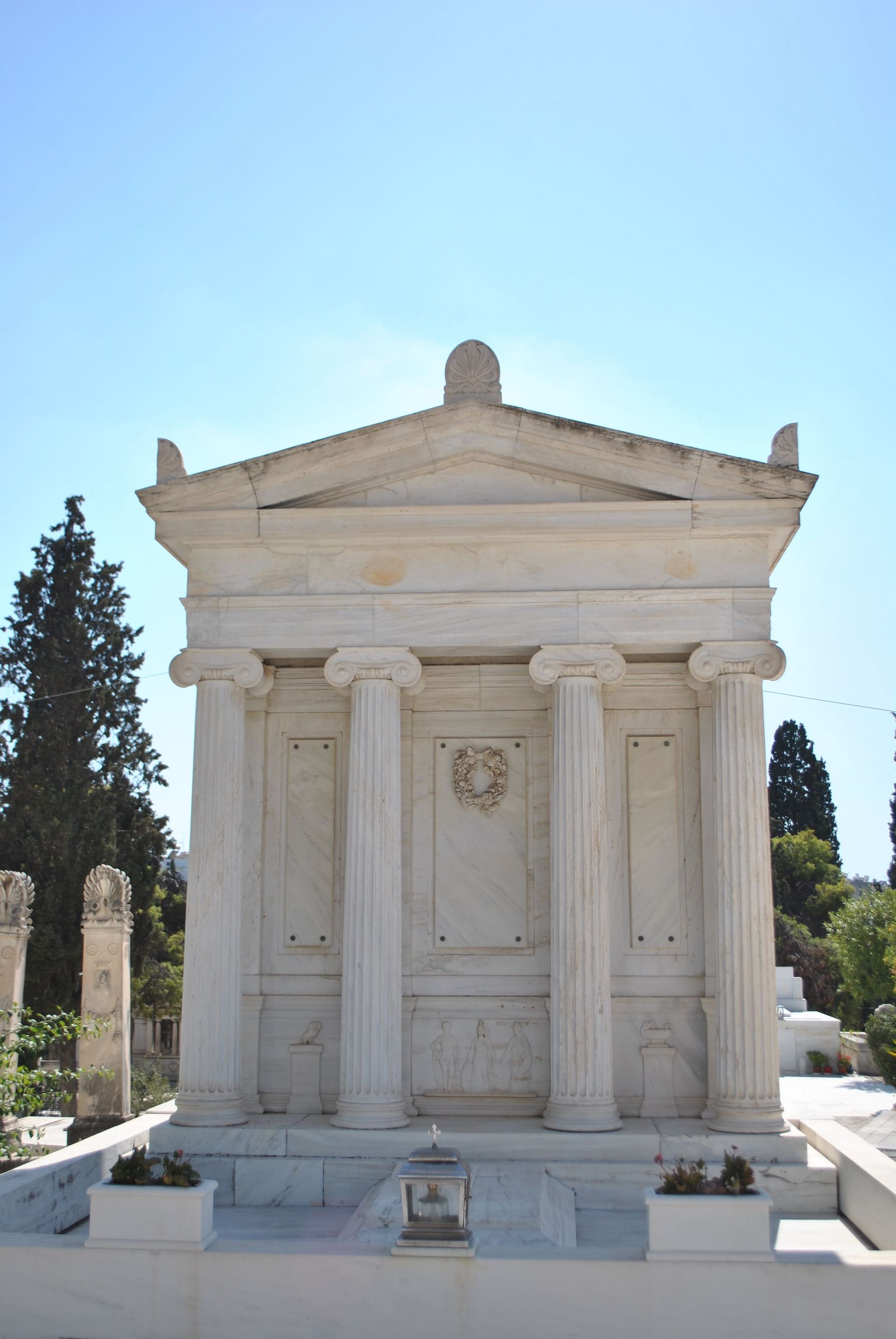 White marble mausoleum with columns and a triangular pediment in a sunny cemetery