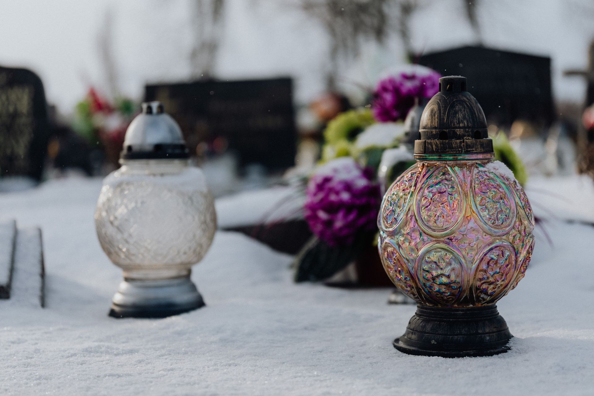 Decorative lanterns on snow at a cemetery, with purple flowers in the background