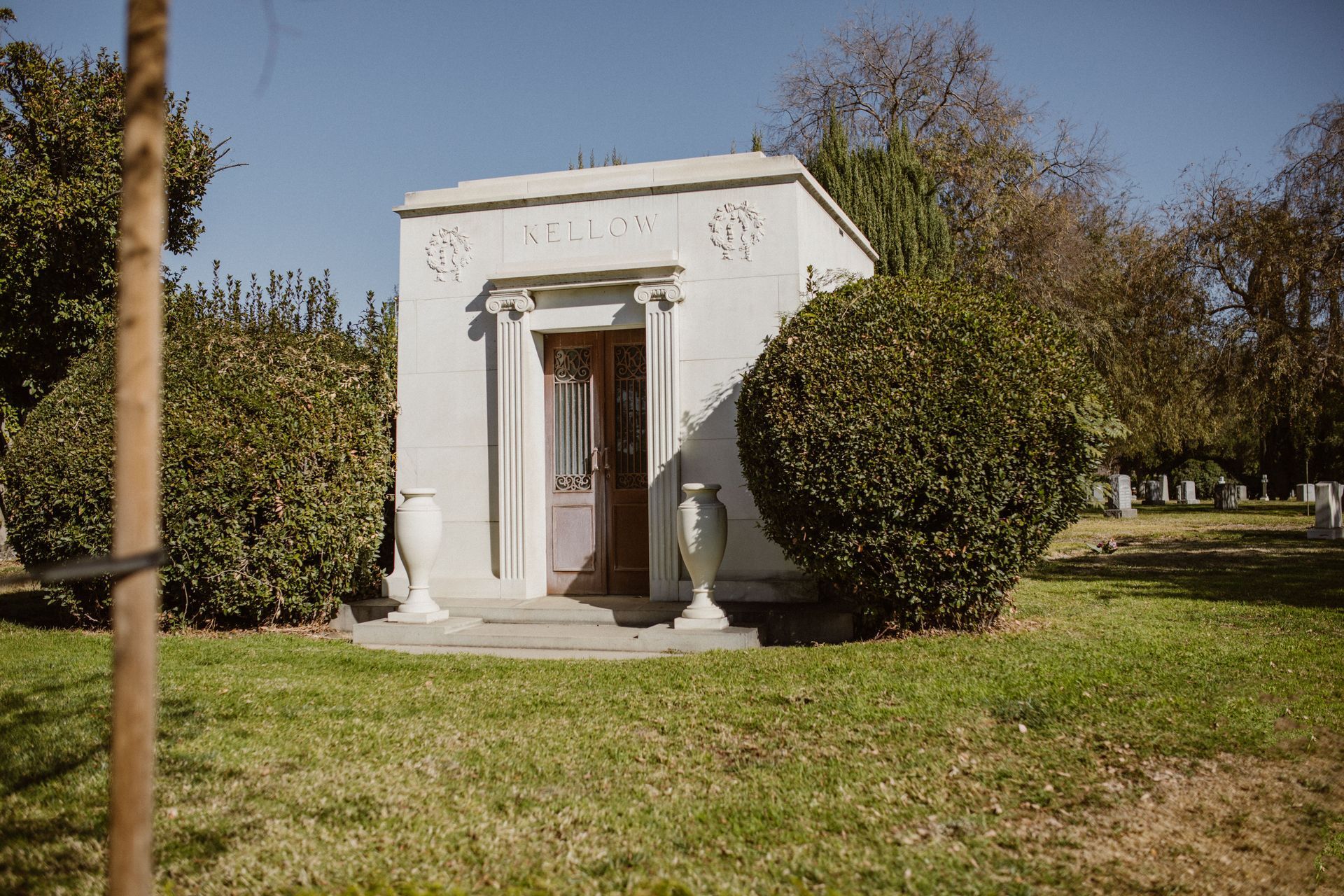 Small white garden pavilion with columns, surrounded by trees and grass in sunlight.
