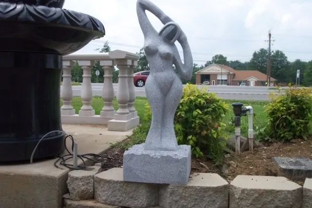 Gray abstract sculpture on a stone base beside a black planter in an outdoor garden area