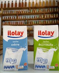 Dos cartones de leche, marca “Iolay”, leche entera (azul) y descremada (verde), en un entorno de tienda.