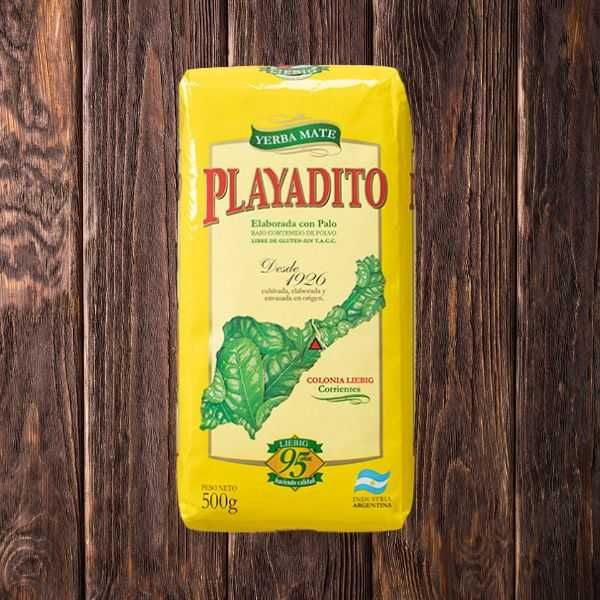 Bolsa de mate Playadito amarilla sobre mesa de madera con diseño de hojas verdes.