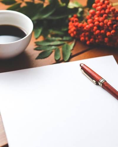 White paper and pen next to coffee and red berries on a wooden table.