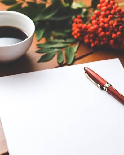 White paper and pen next to coffee and red berries on a wooden table.