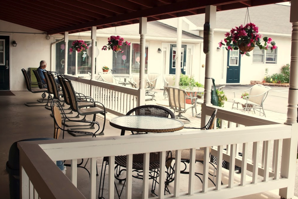 A porch with tables and chairs and flowers hanging from the ceiling