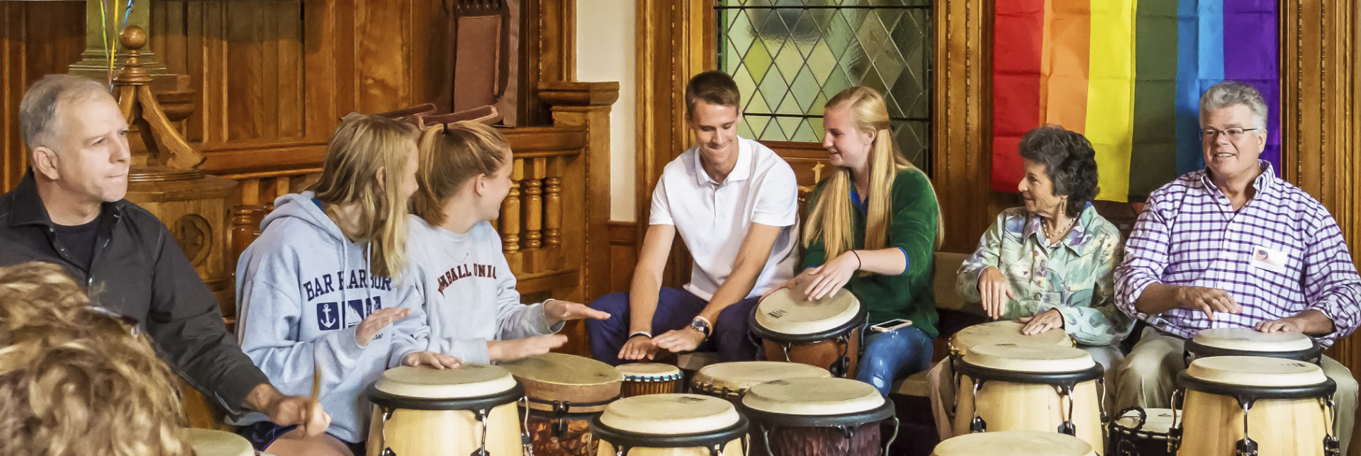 A group of people are playing drums in front of a rainbow flag