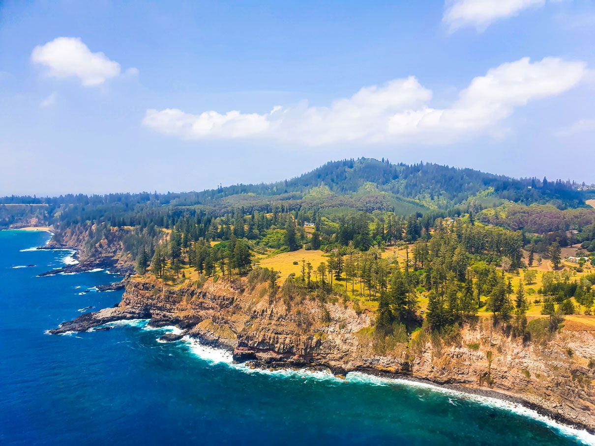 Rocky coastline with lush trees and blue ocean under a bright sky. Norfolk Island Trade Winds Seniors Sanctuary