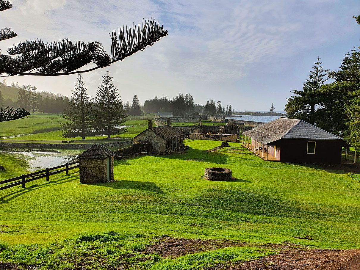 Green field with old stone buildings under a cloudy sky. Norfolk Island Trade Winds Seniors Sanctuary