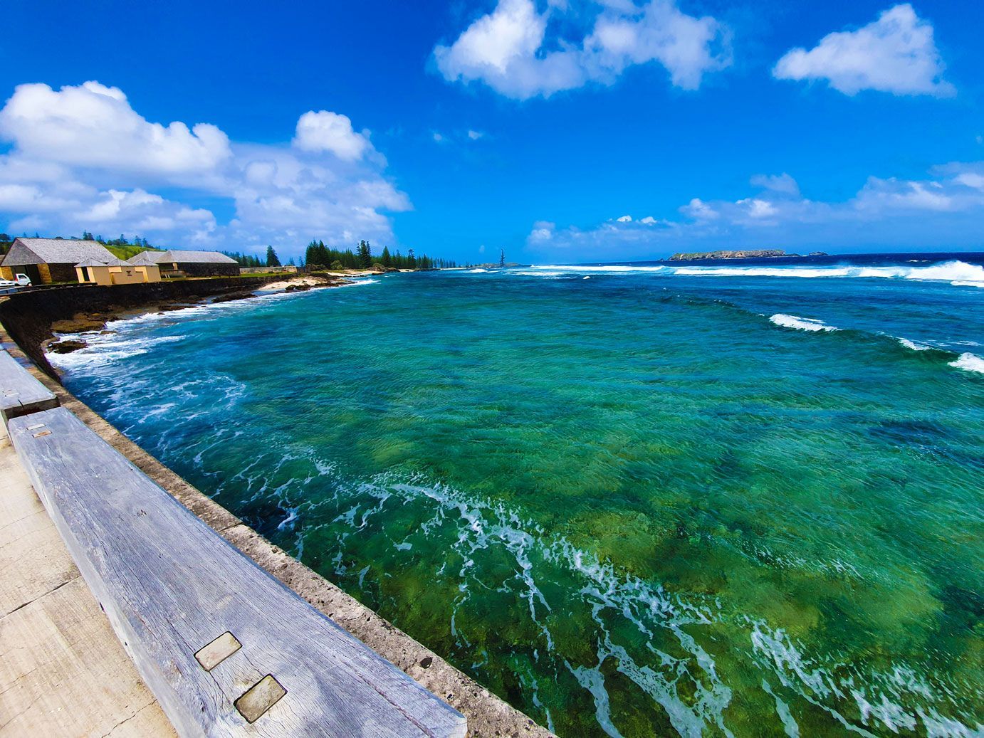 Azure ocean waves crash against a rocky coast under a blue sky. Norfolk Island Trade Winds Seniors Sanctuary