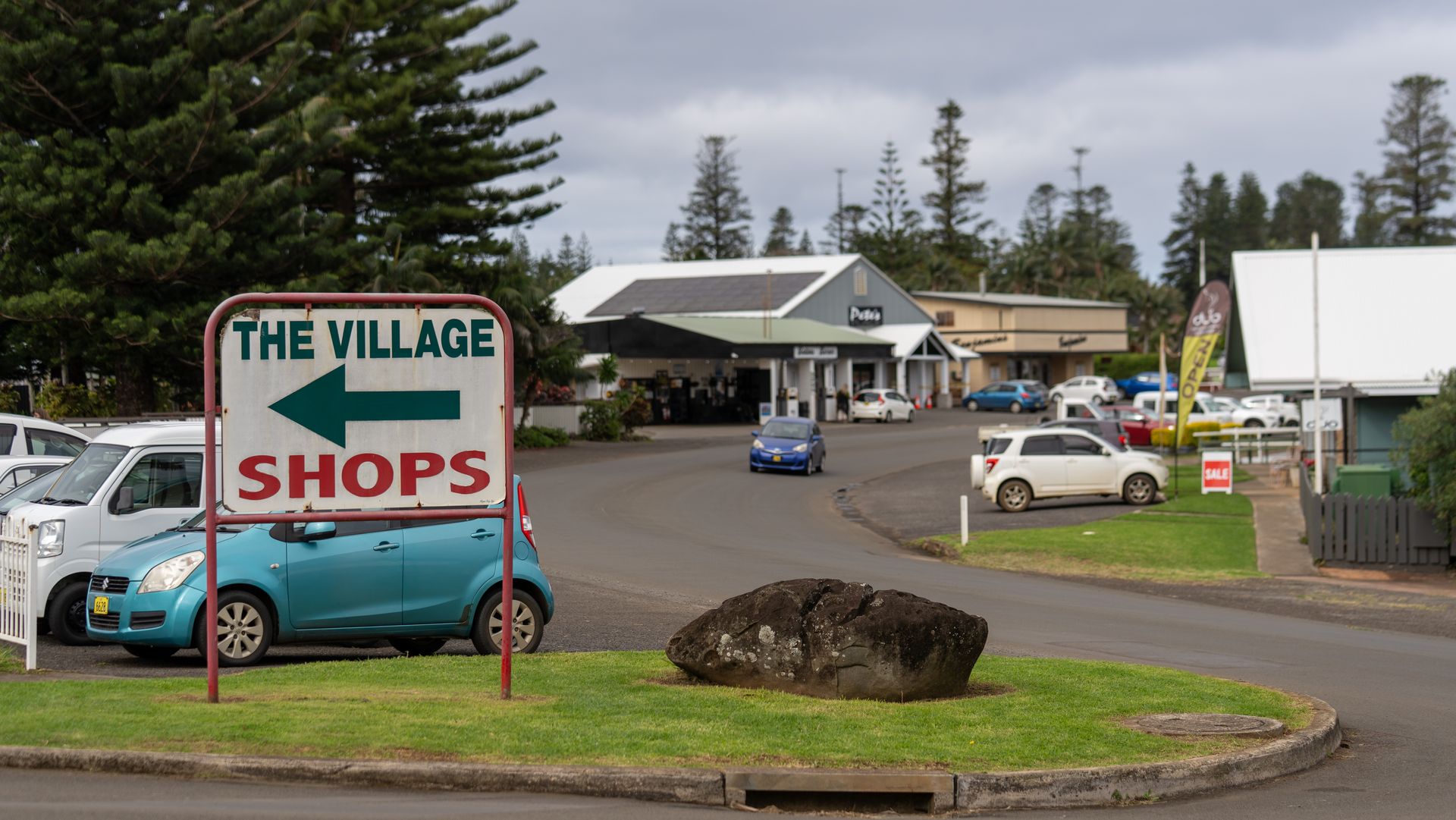 The Village Shops sign beside a parking lot and buildings on an overcast day.
