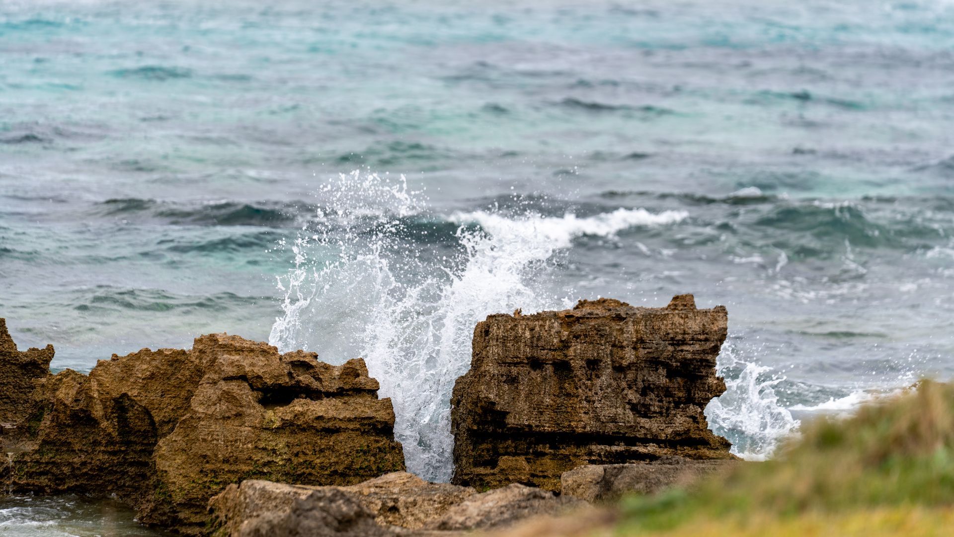 Waves crashing against rocky shoreline under a gray sky