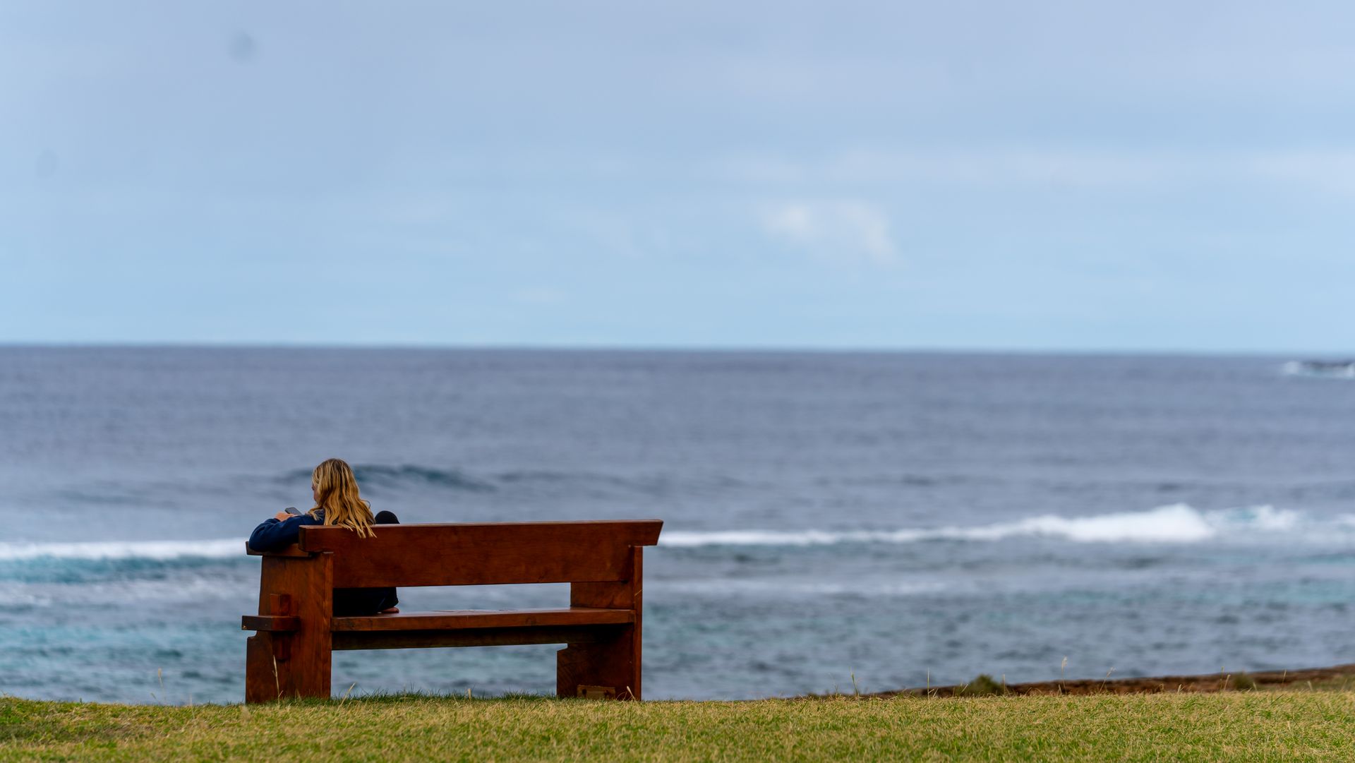 Wooden bench on a grassy cliff overlooking the ocean under a cloudy sky