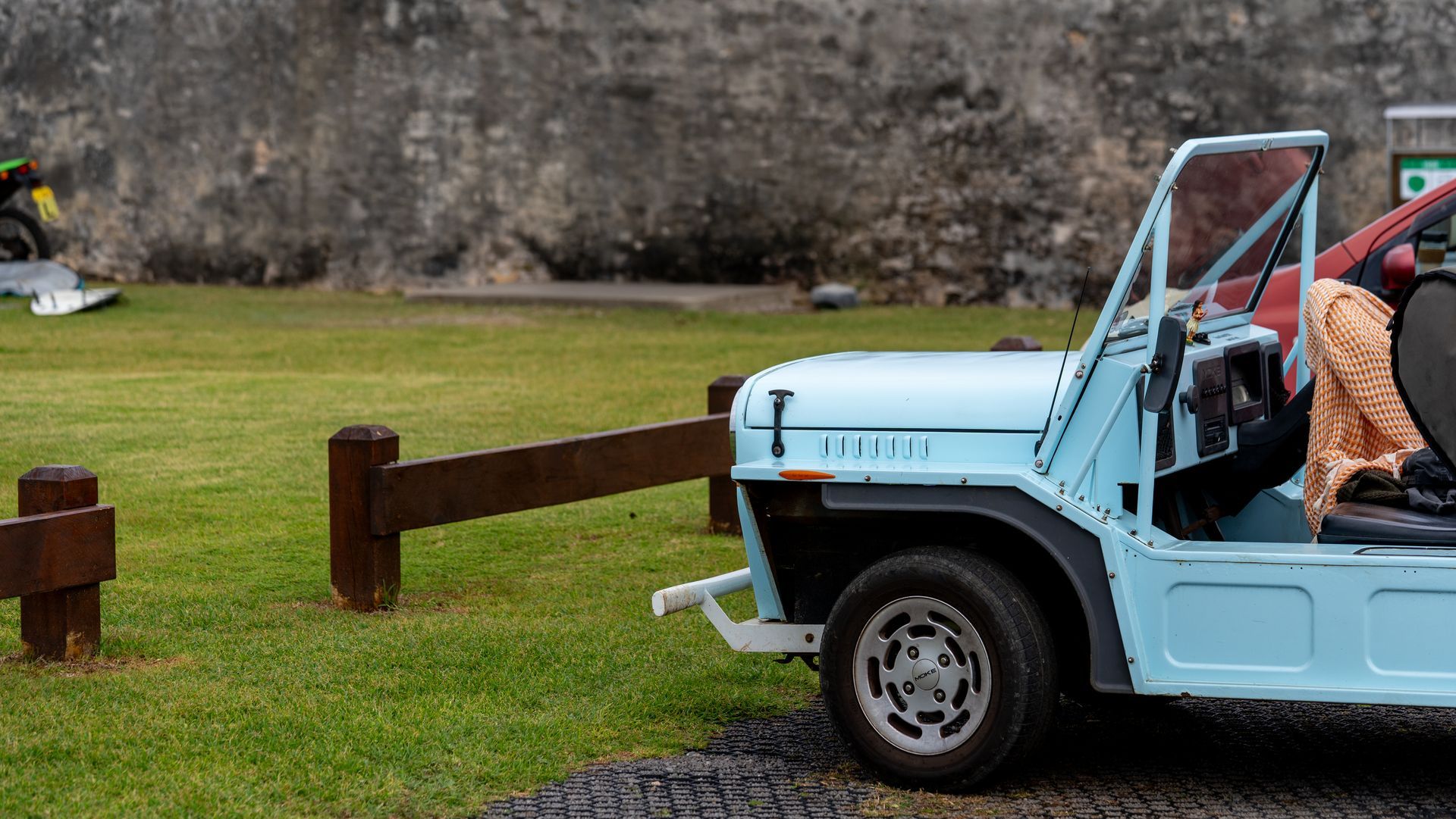 Light blue off-road vehicle parked on grass beside wooden posts, with a person seated inside