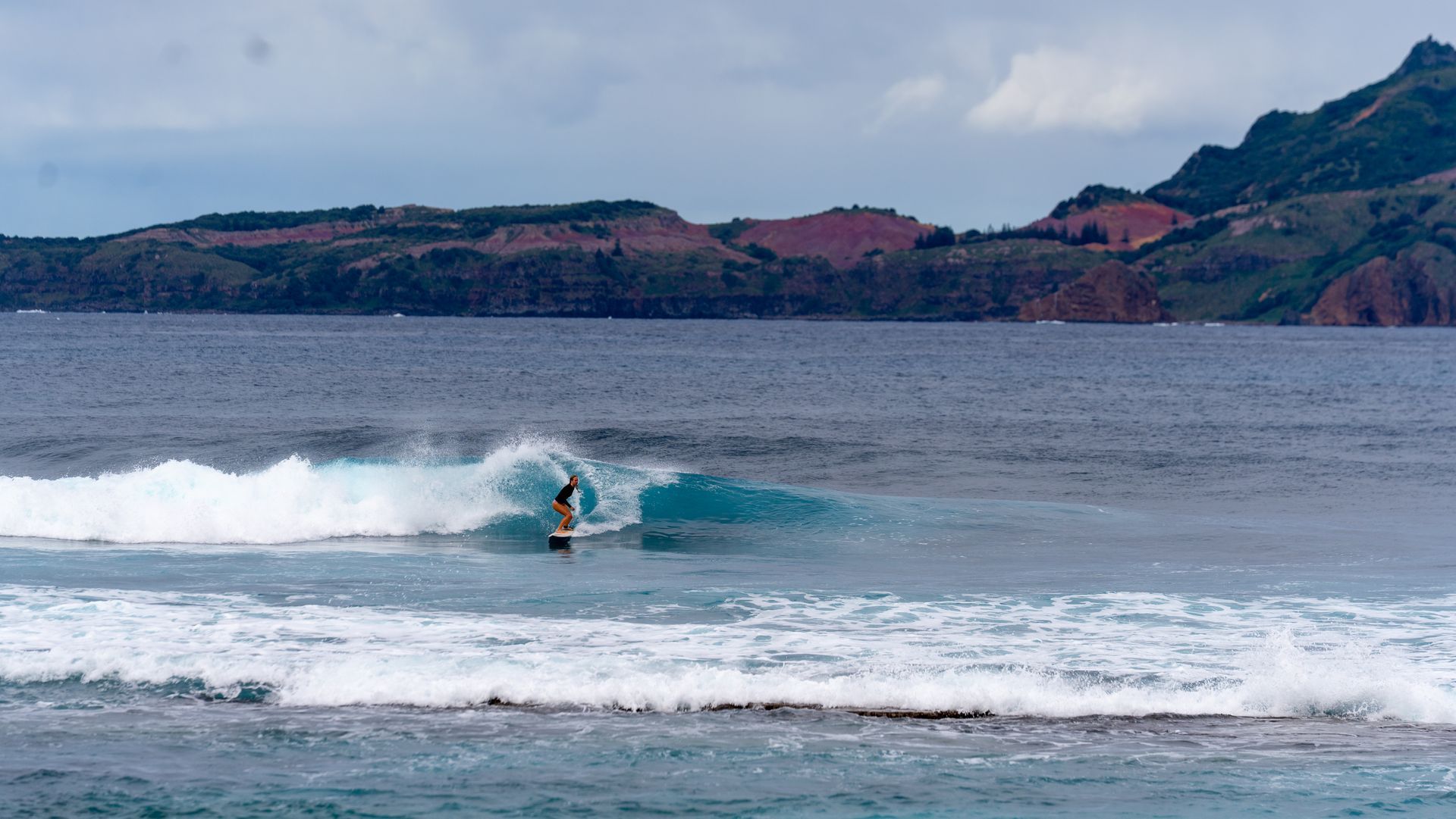 Surfer riding a wave near a rocky coastline under a cloudy sky