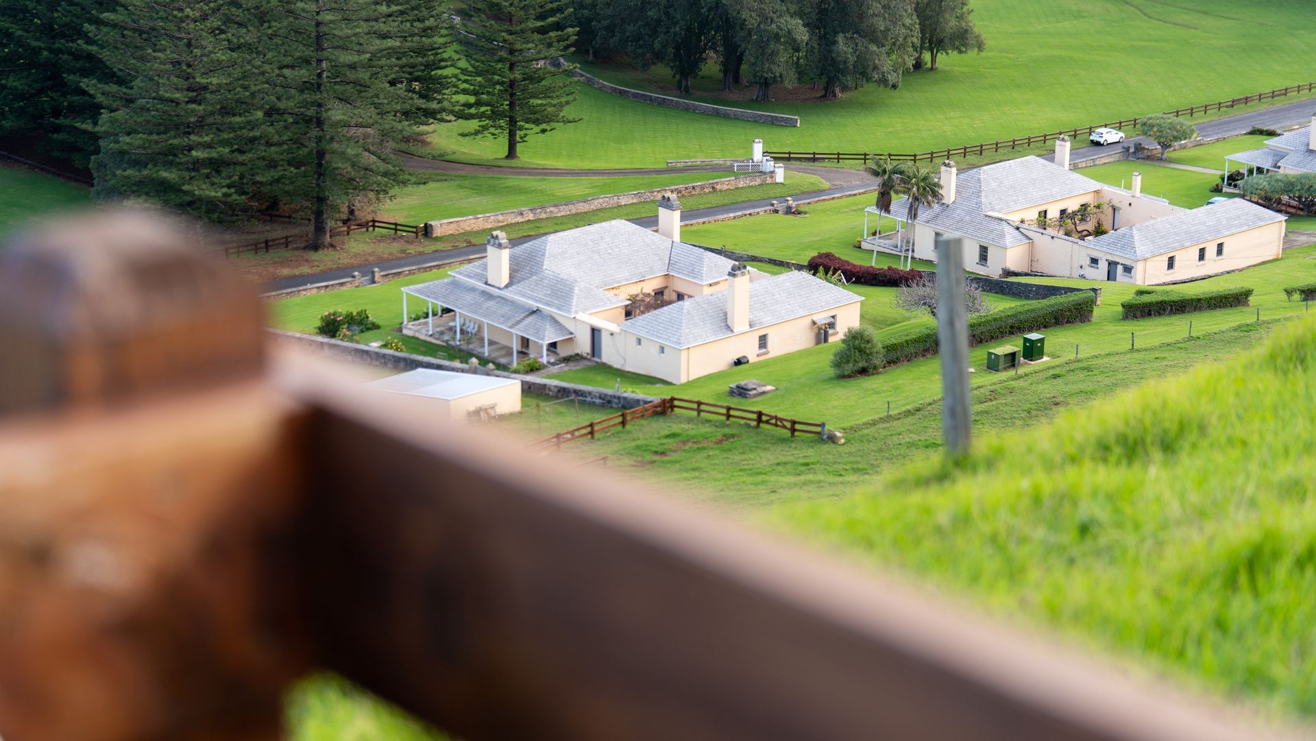 White cottages in a green hillside valley, viewed from a blurred wooden fence in the foreground