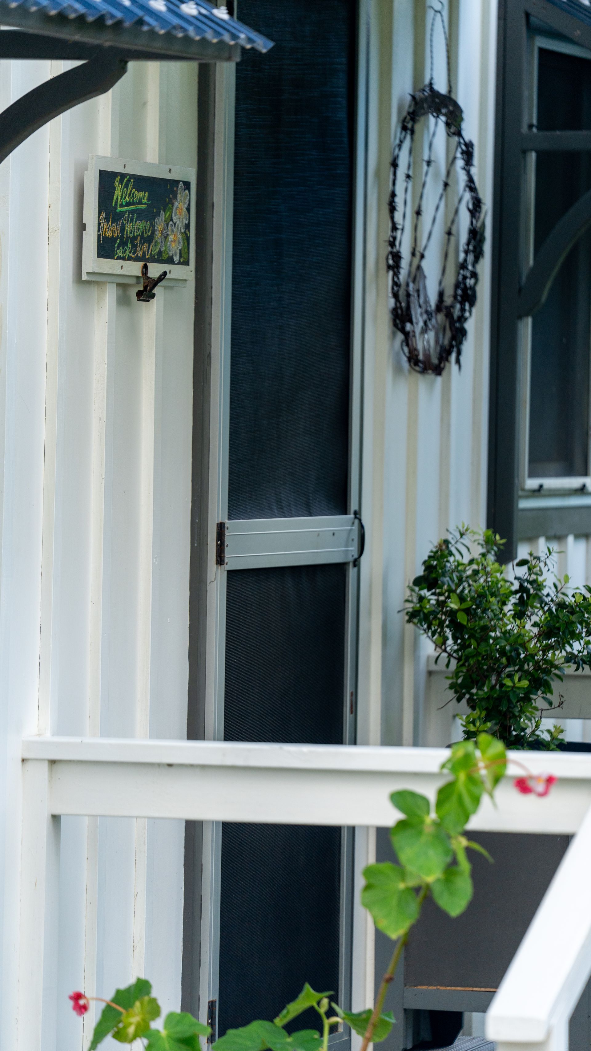 White house exterior with screened door, black wreath, and small hanging plant.