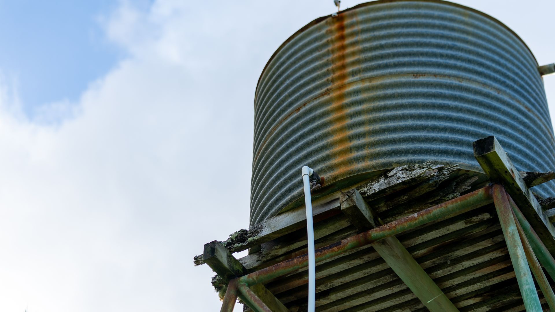 Large corrugated metal water tank on a raised wooden platform against a blue sky