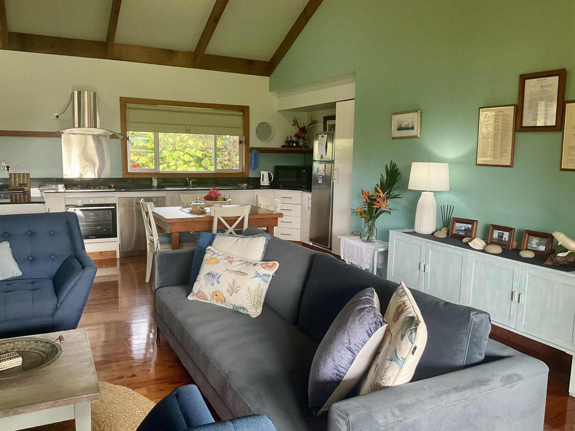 Living room with gray sofa, blue armchairs, and open kitchen. Norfolk Island Trade Winds Seniors Sanctuary
