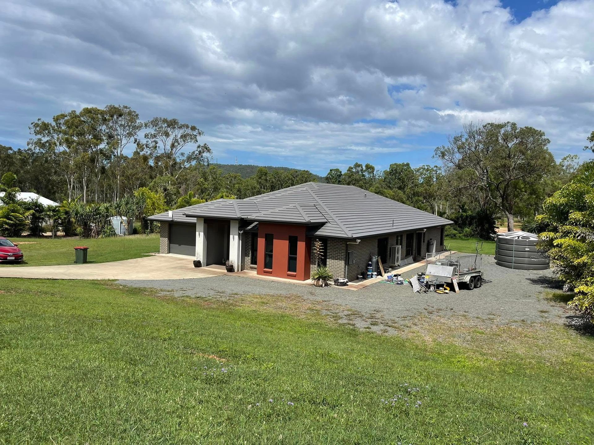 House With Dark Roof and Red Accents Sits on a Grassy Lot With Gravel Driveway — Roof Tek CQ in Rockhampton, QLD