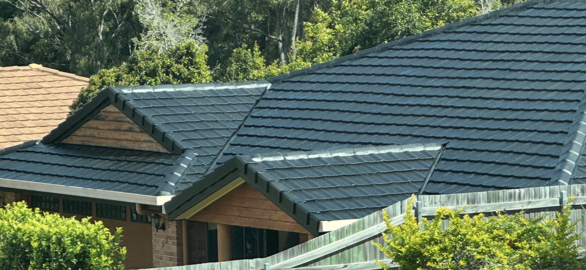 Dark gray tiled roof on a house with a triangular section, trees in the background, and a fence in the foreground — Roof Tek CQ in Gracemere, QLD