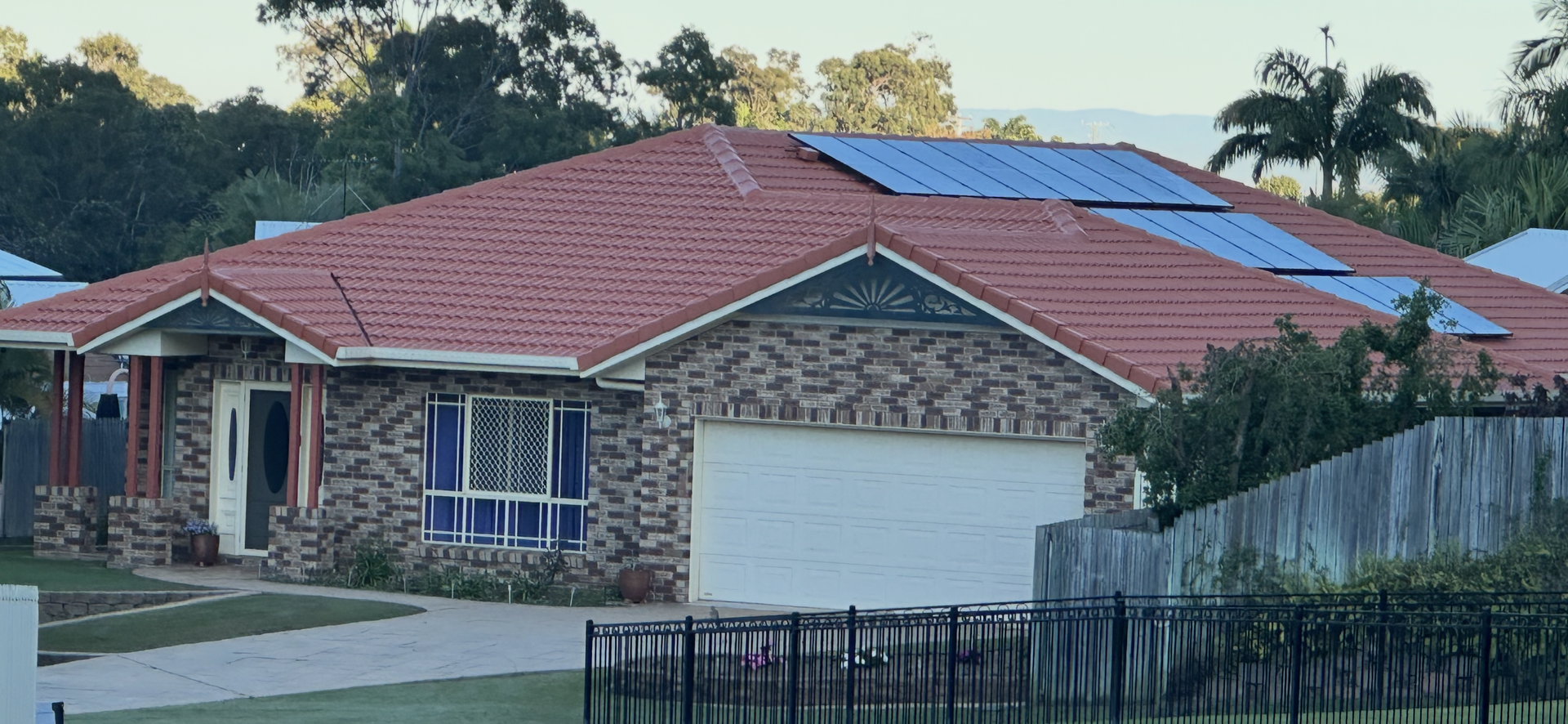 Residential house with red tile roof, brick facade, and solar panels. White garage door, blue-tinted windows — Roof Tek CQ in Gracemere, QLD