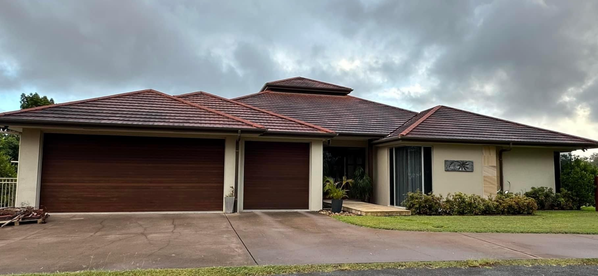 A house with a dark brown garage door, brown roof, and front lawn under a cloudy sky — Roof Tek CQ in Gracemere, QLD