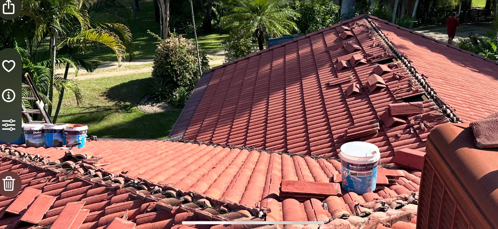 Red tile roof with broken sections, paint buckets, and surrounding greenery