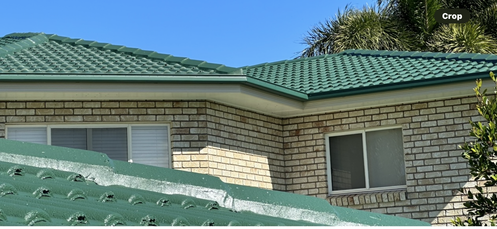 Green tile roof on a brick house against a blue sky — Roof Tek CQ in Gracemere, QLD