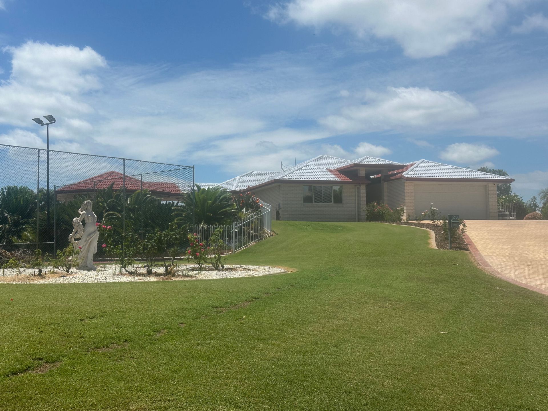 House with a red-tiled roof, green lawn, white fence, and blue sky with clouds — Roof Tek CQ in Gracemere, QLD