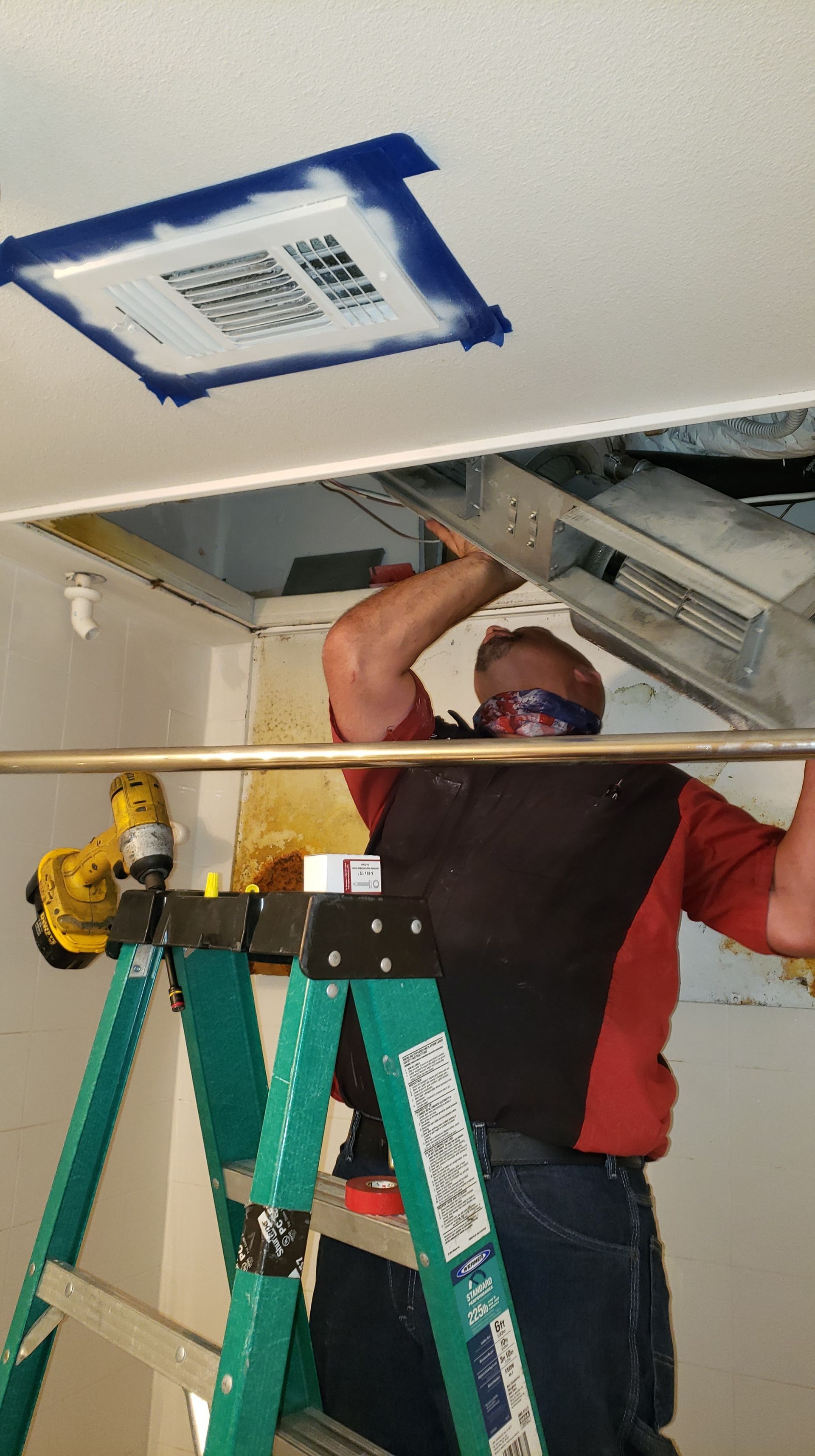 A man is standing on a ladder working on a ceiling.