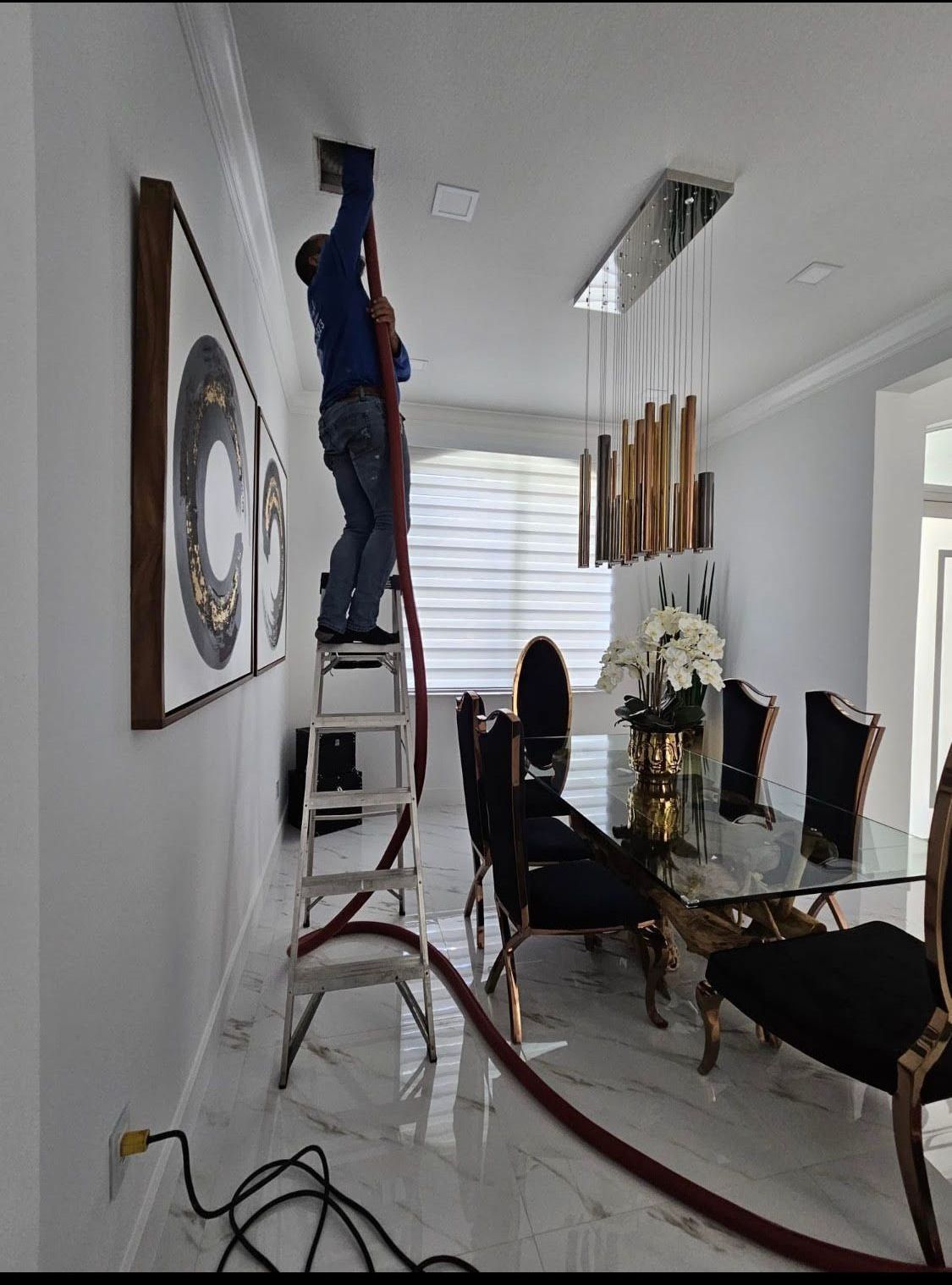 Person cleaning air duct in a dining room, using a ladder and hose.