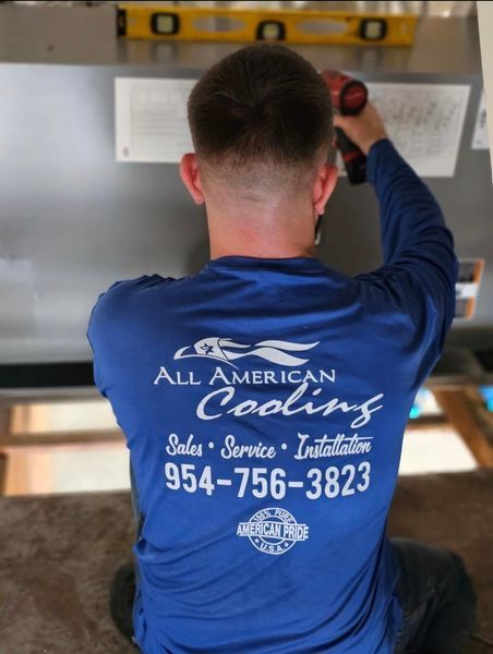 Technician installing something overhead, wearing blue shirt with 
