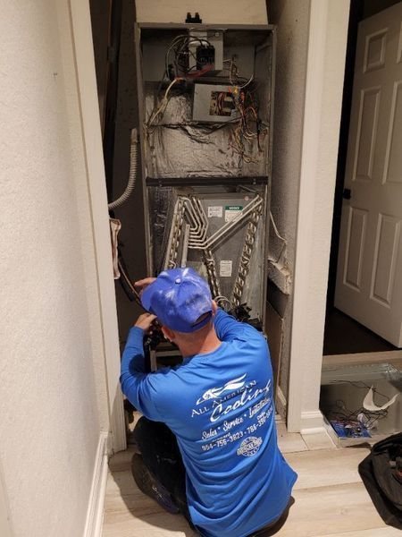 A person in a blue shirt is working on an electrical panel in a small room.