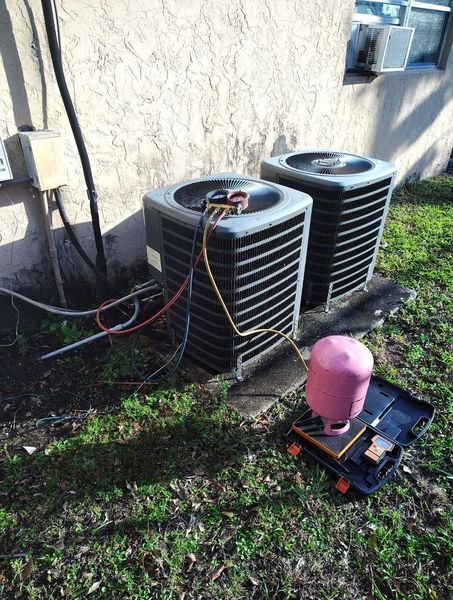 Two AC units outside a building with a pink refrigerant tank nearby.