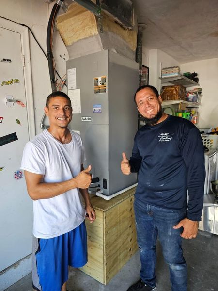 Two men giving thumbs-up next to new HVAC unit in a garage.