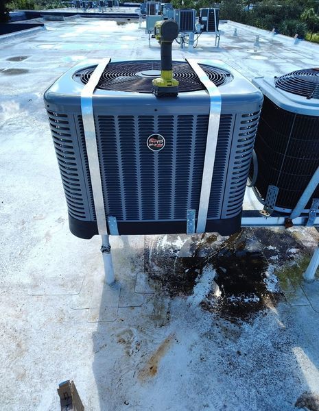 HVAC unit on a rooftop, secured with metal straps. A drill sits on top; white roof.