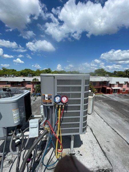 AC unit on a rooftop, with gauges attached. Blue sky and clouds in the background.