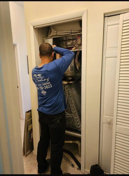 Man in blue shirt works on an HVAC system inside a closet.