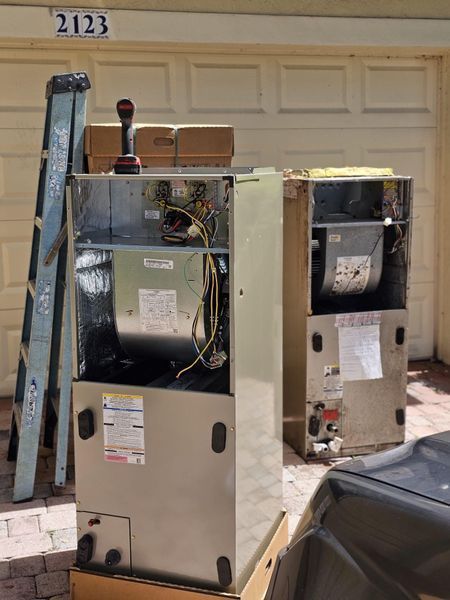 Two HVAC units outside a garage; one open, with tools and a ladder.