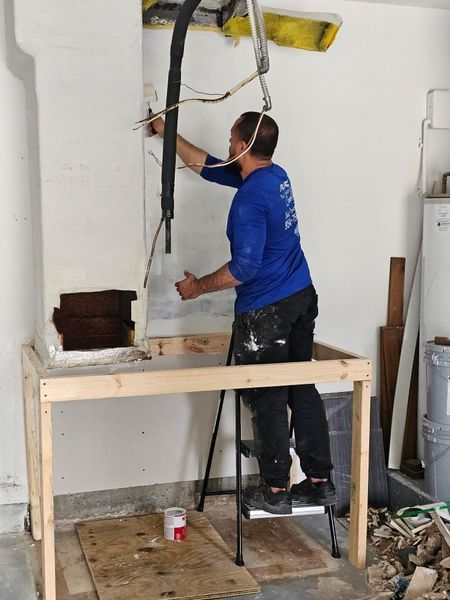 Man in blue shirt works on electrical wiring above a wooden work table in a room.