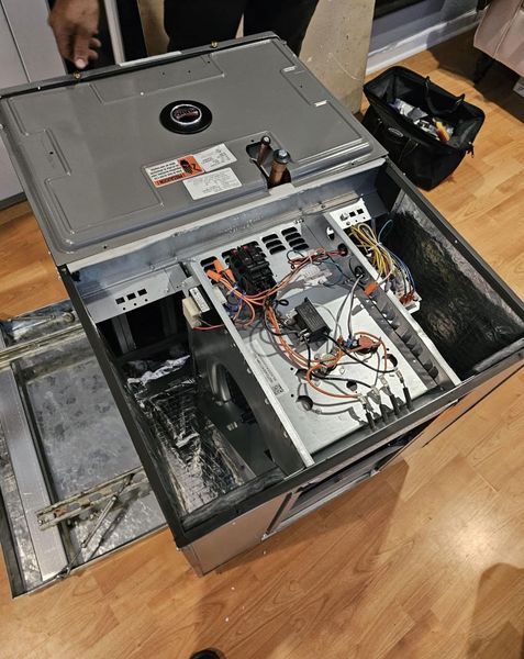 HVAC unit with the top open, showing wires and internal components on a wood floor.