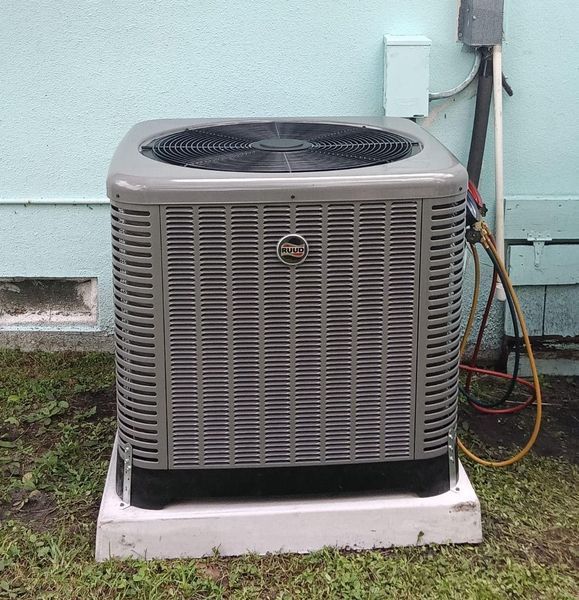 An air conditioning unit on a concrete pad outside a light blue building.